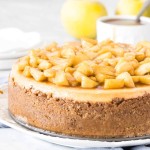 Round cheesecake topped with chopped cinnamon apples on a plate.