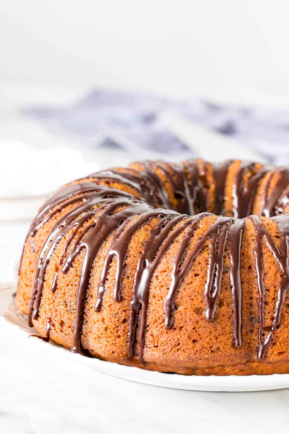 Pumpkin bundt cake on a plate, drizzled with chocolate ganache. 