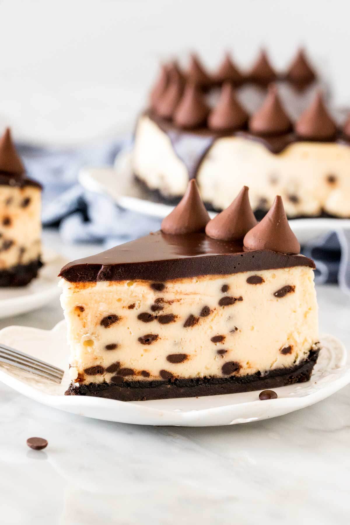 Slice of chocolate chip cheesecake on a plate with cheesecake in background. 