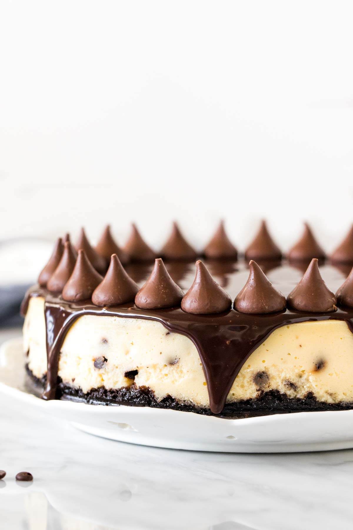 Cheesecake with cookie crust, chocolate topping and chocolate kisses on a round plate. 