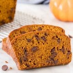 Slices of pumpkin chocolate chip bread beside half a loaf on a cooling rack.