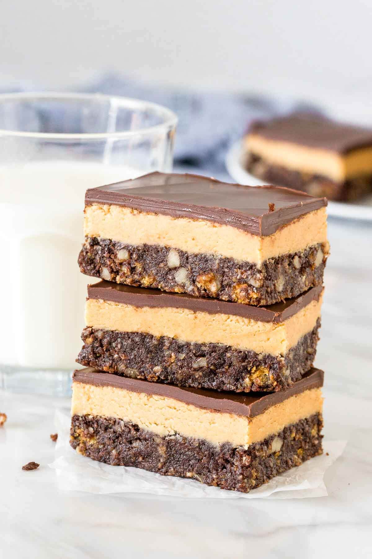 A stack of 3 peanut butter nanaimo bars with a glass of milk. 