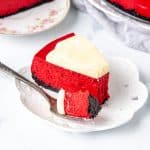 Piece of red cheesecake with cream cheese frosting and an Oreo crust