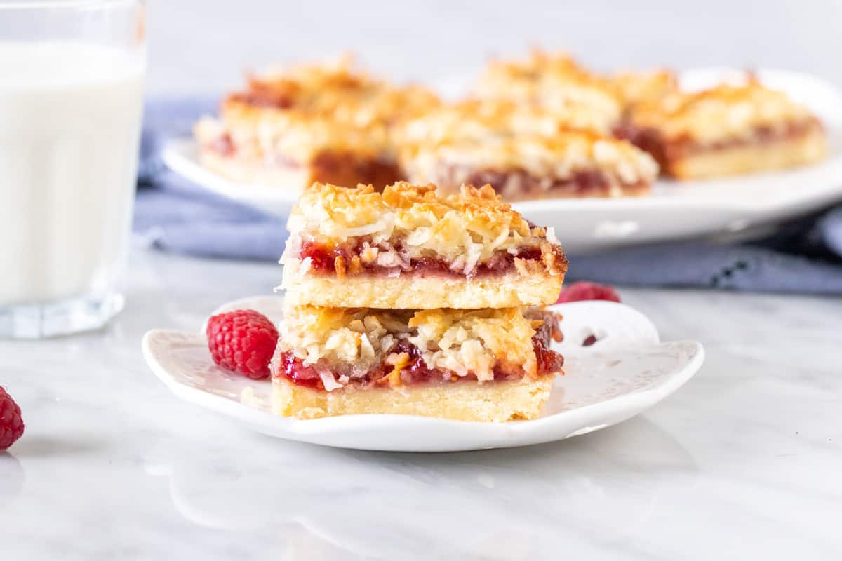 2 raspberry jam bars with coconut topping, stacked on a plate.