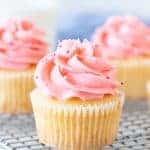 Vanilla cupcakes with pink frosting on cooling rack.