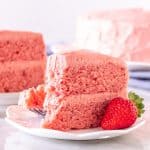 Slice of strawberry cake with strawberry frosting on a plate.