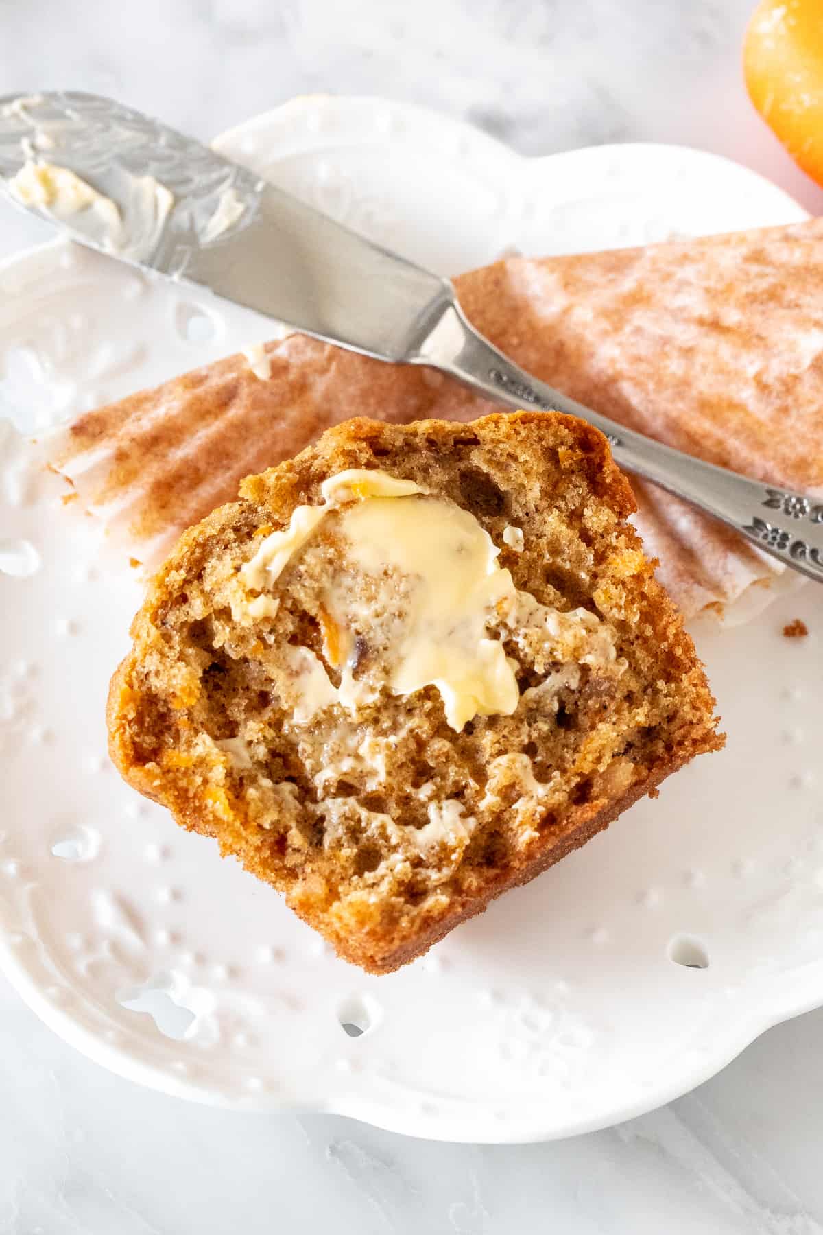 Half a carrot cake muffin with butter on it.