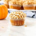 Pumpkin streusel muffin with glaze on top, with a plate of muffins in the background.