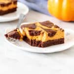 Swirled pumpkin cheesecake brownie on a plate with a bite taken out.