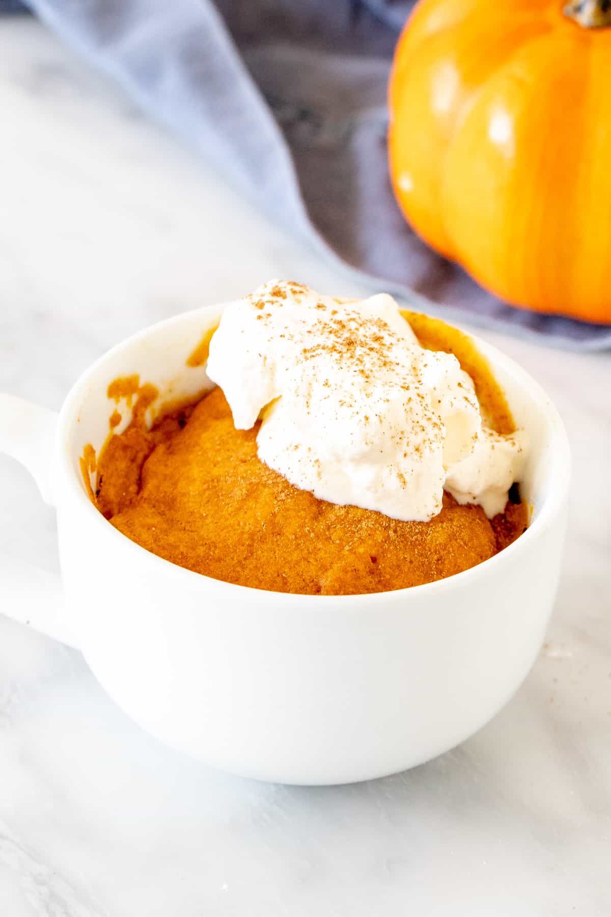 Pumpkin mug cake in a white teacup with whipped cream on top