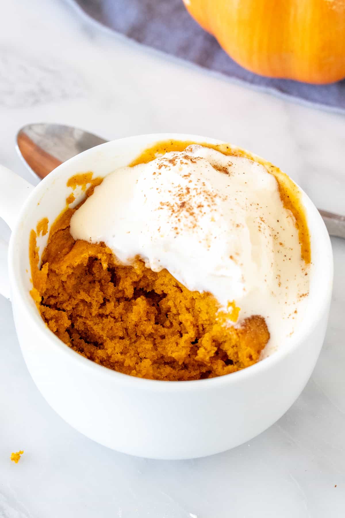Pumpkin cake in a mug, with a bite taken out and topped with melted whipped cream