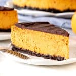 Slice of chocolate pumpkin cheesecake with full cheesecake in the background