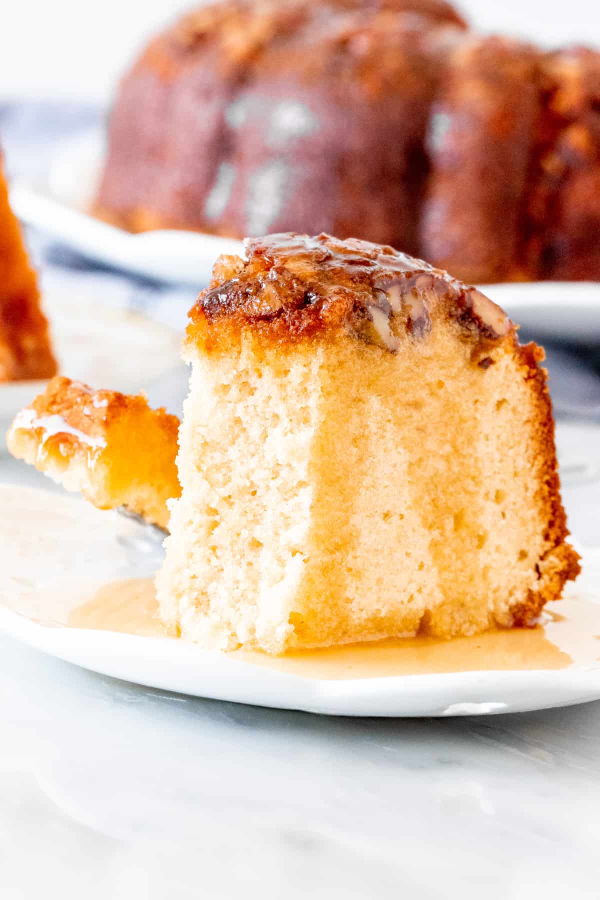Piece of bunt cake with nuts on top and rum sauce poured over top.