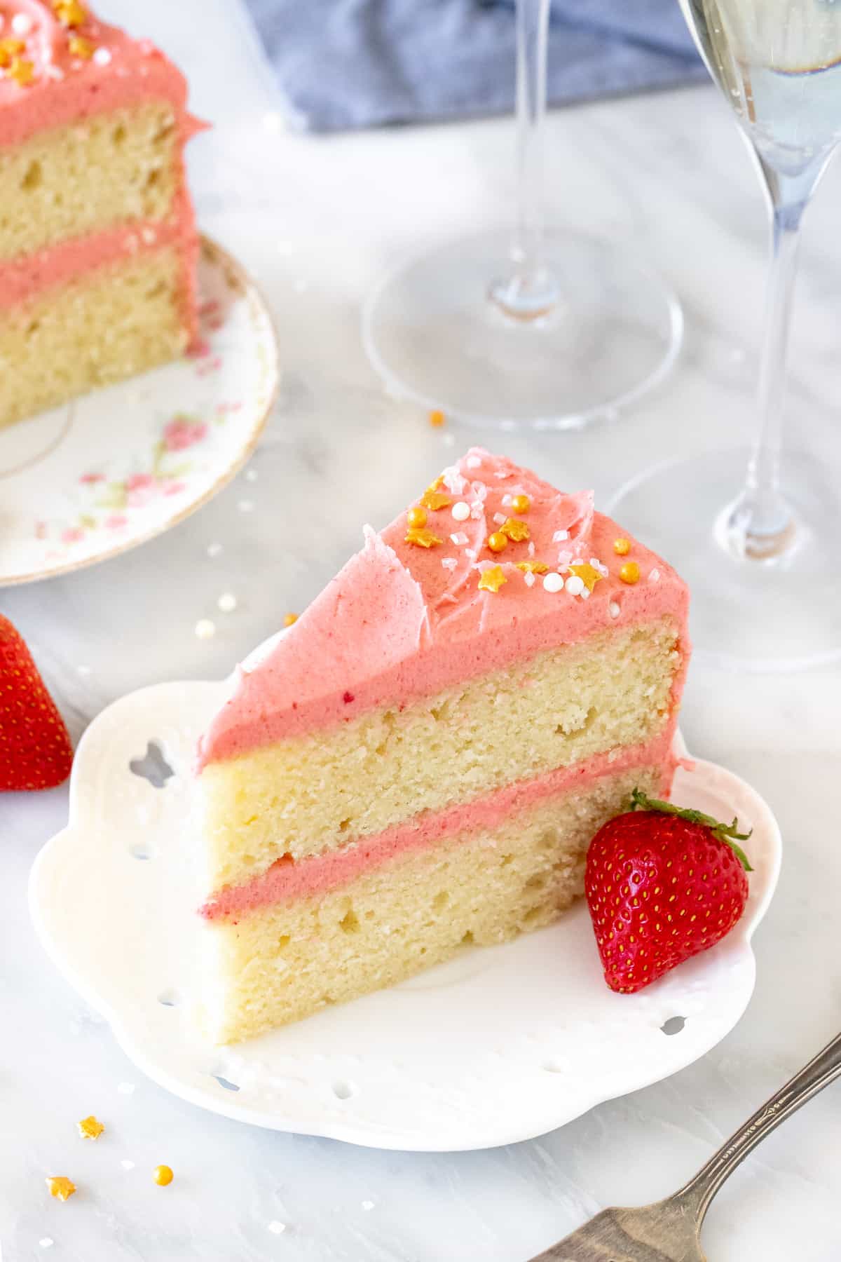 Slice of cake with pink frosting with 2 glasses of sparkling wine