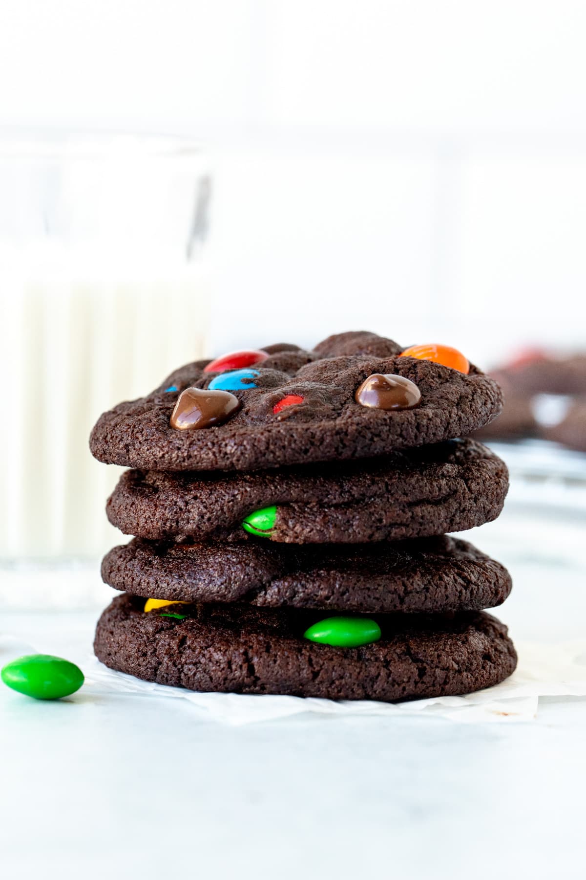M&M chocolate cookies, placed on on top of each other with glass of milk