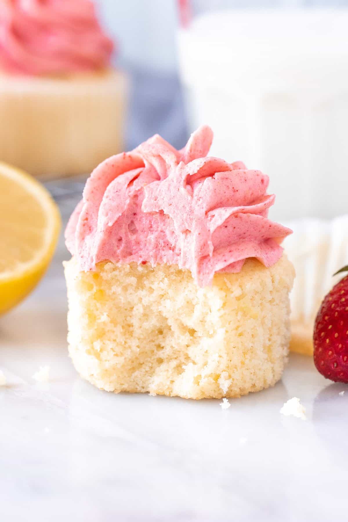 Strawberry lemonade cupcake with a bite taken out with a glass of milk