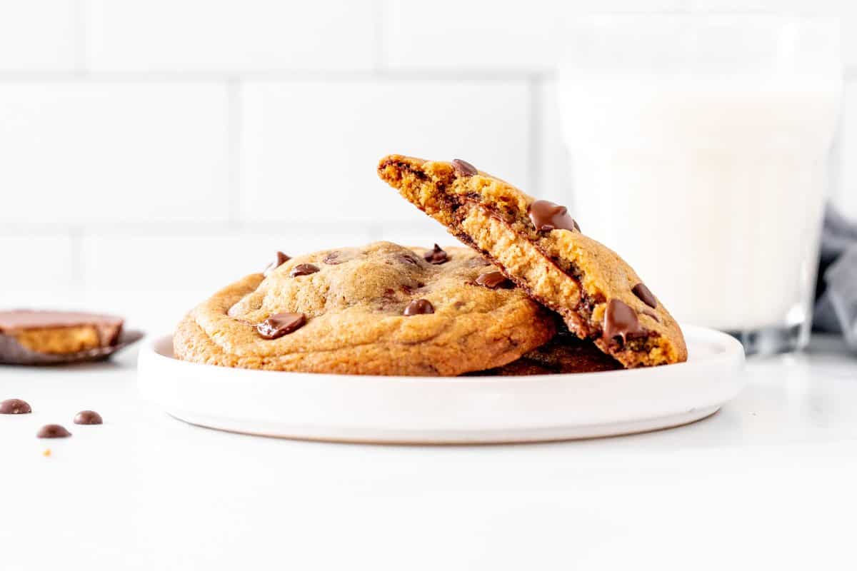 Plate of reese's chocolate chip cookies with 1 cookie broken in half and a glass of milk.
