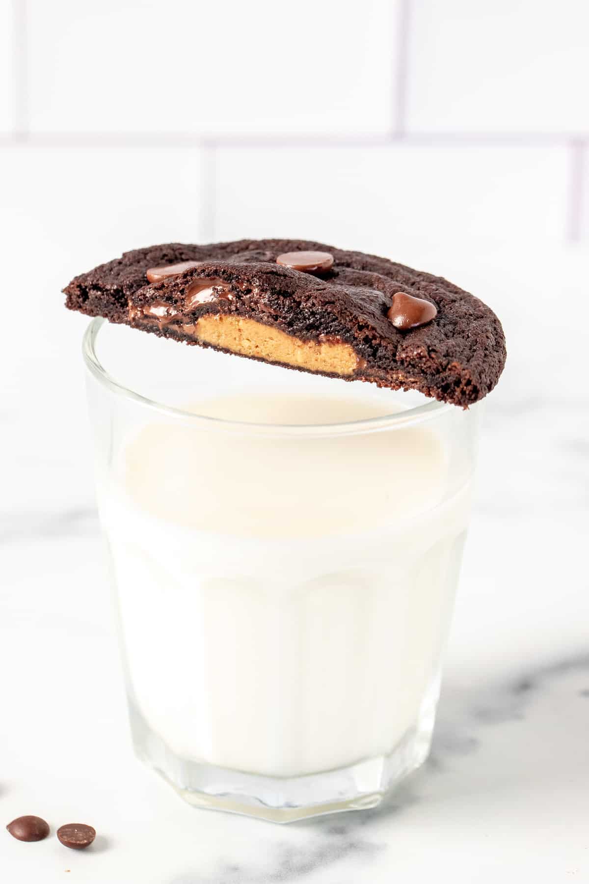 Glass of milk with half a peanut butter cup chocolate cookie on top