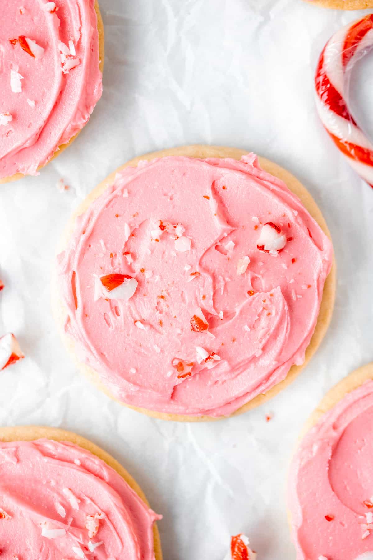 Frosted sugar cookies topped with crushed candy canes on baking paper