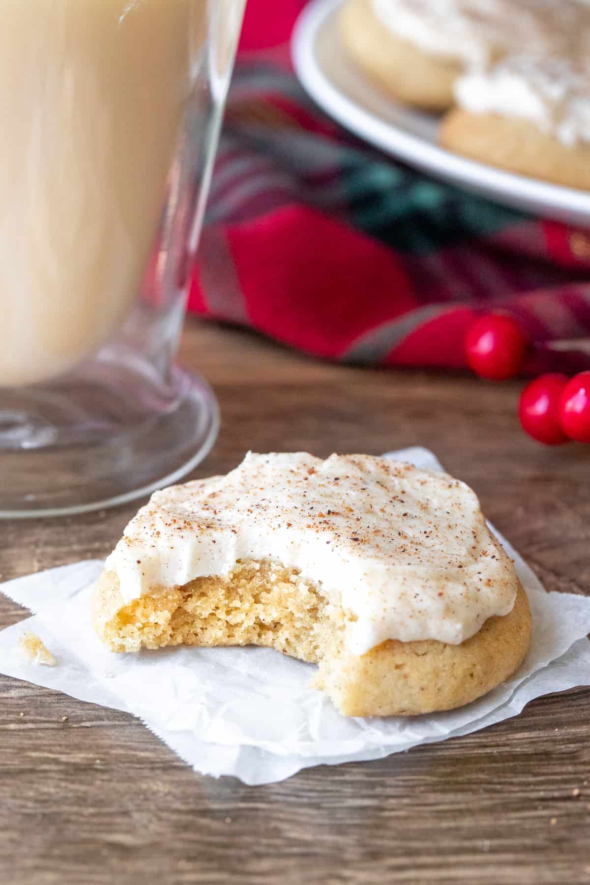 Frosted eggnog cookie with a bite taken out beside a glass of eggnog