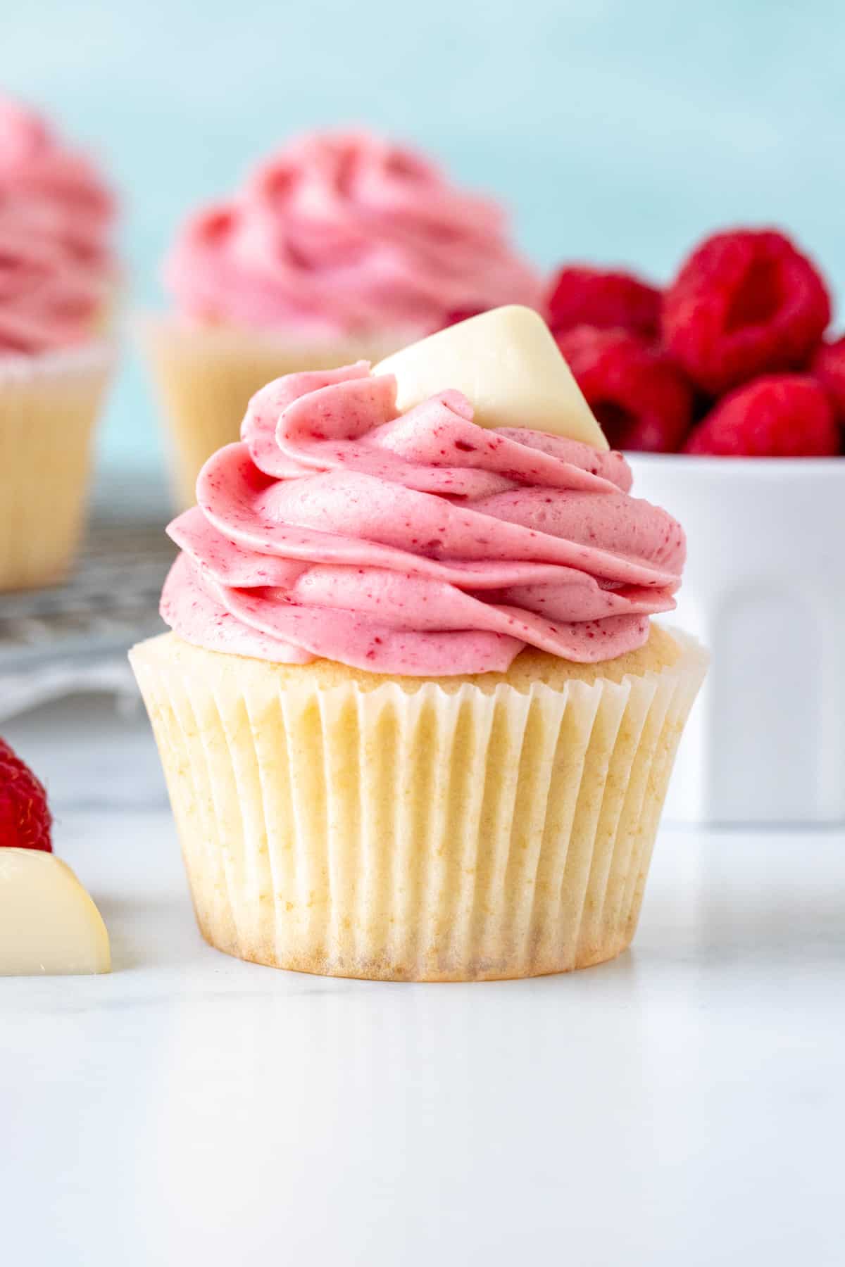 White chocolate raspberry cupcake with small bowl of berries