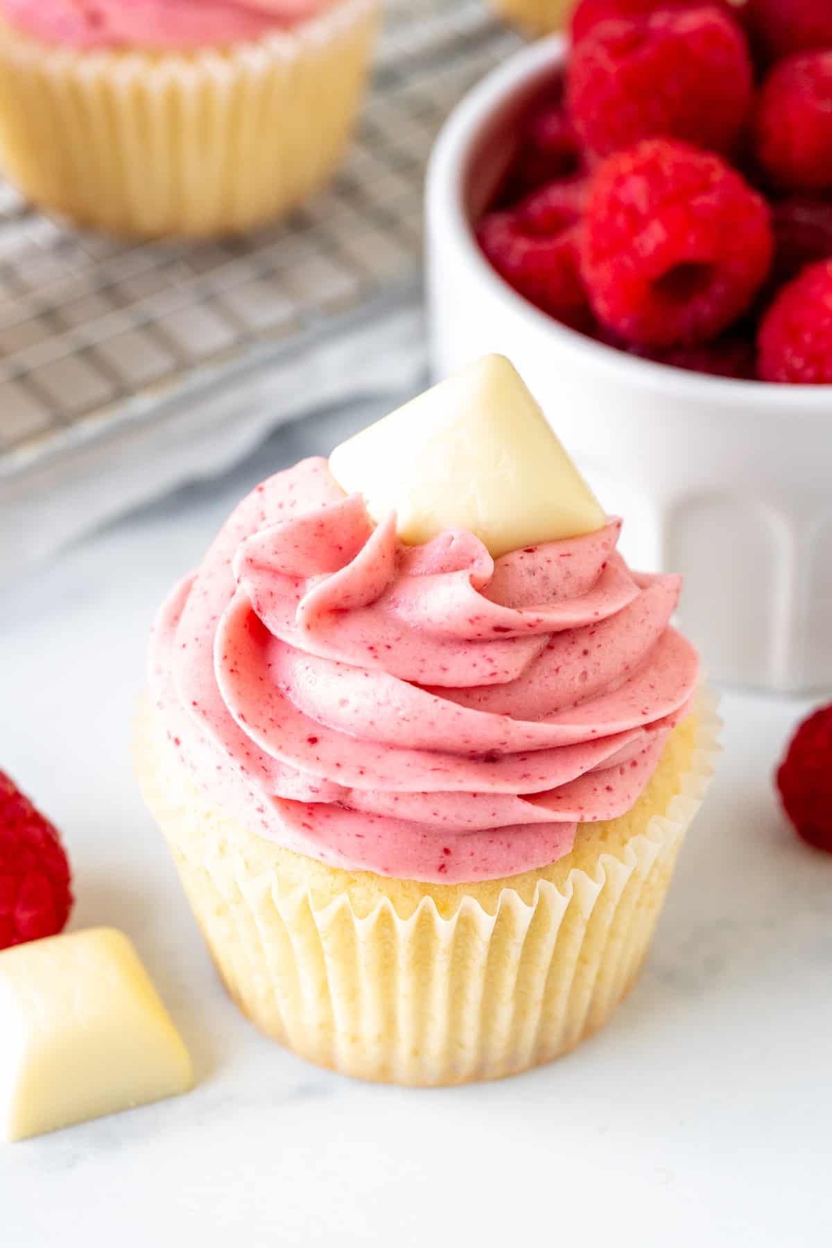 White chocolate cupcake with white chocolate raspberry frosting and topped with square of white chocolate 