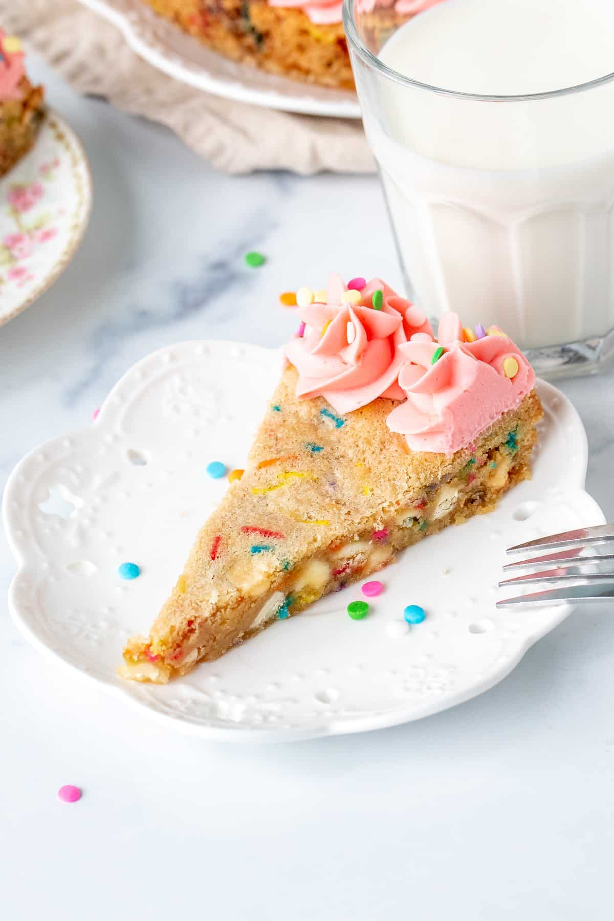 Slice of sprinkle sugar cookie cake with pink frosting