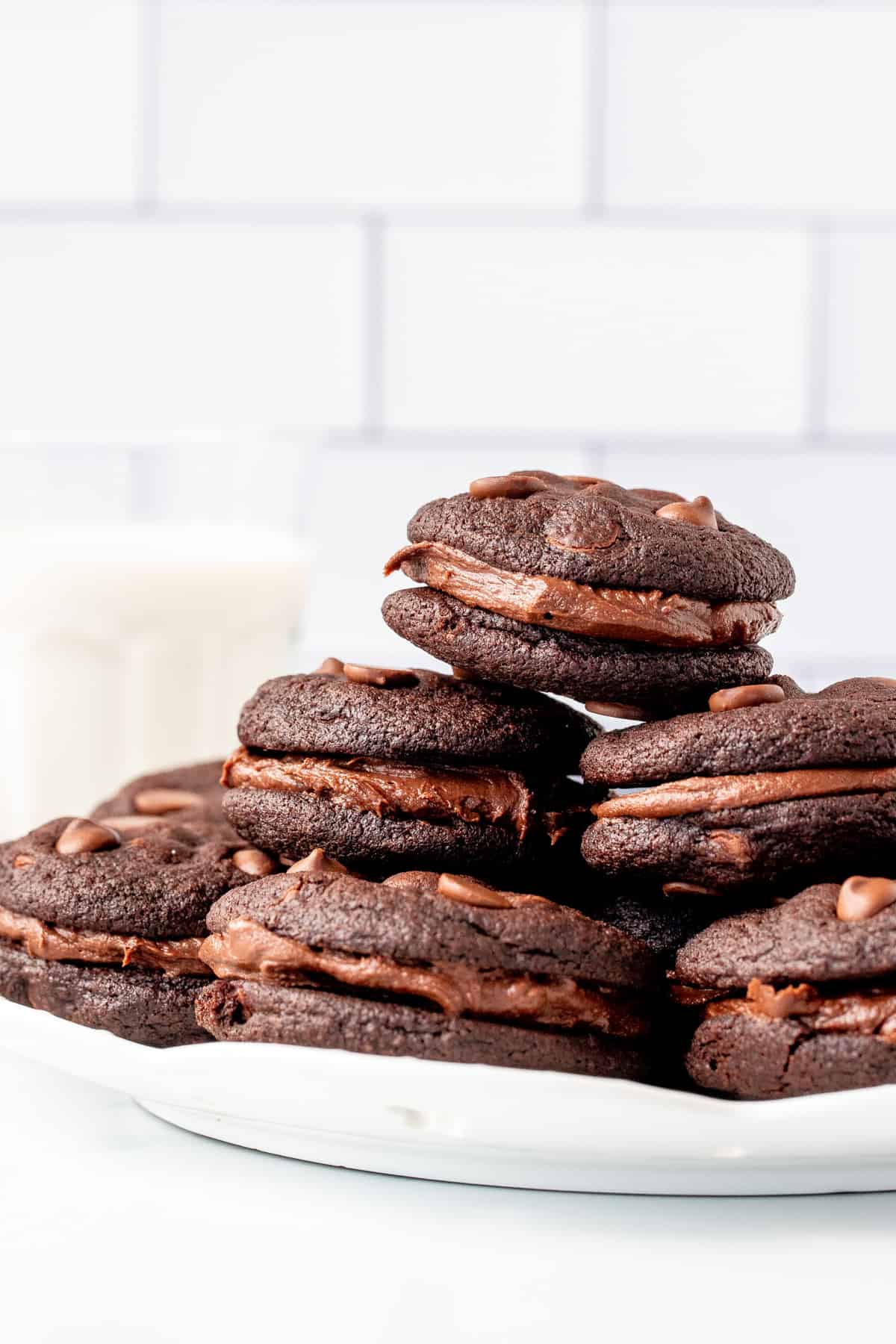 Plate of chocolate sandwich cookies with chocolate frosting with glass of milk