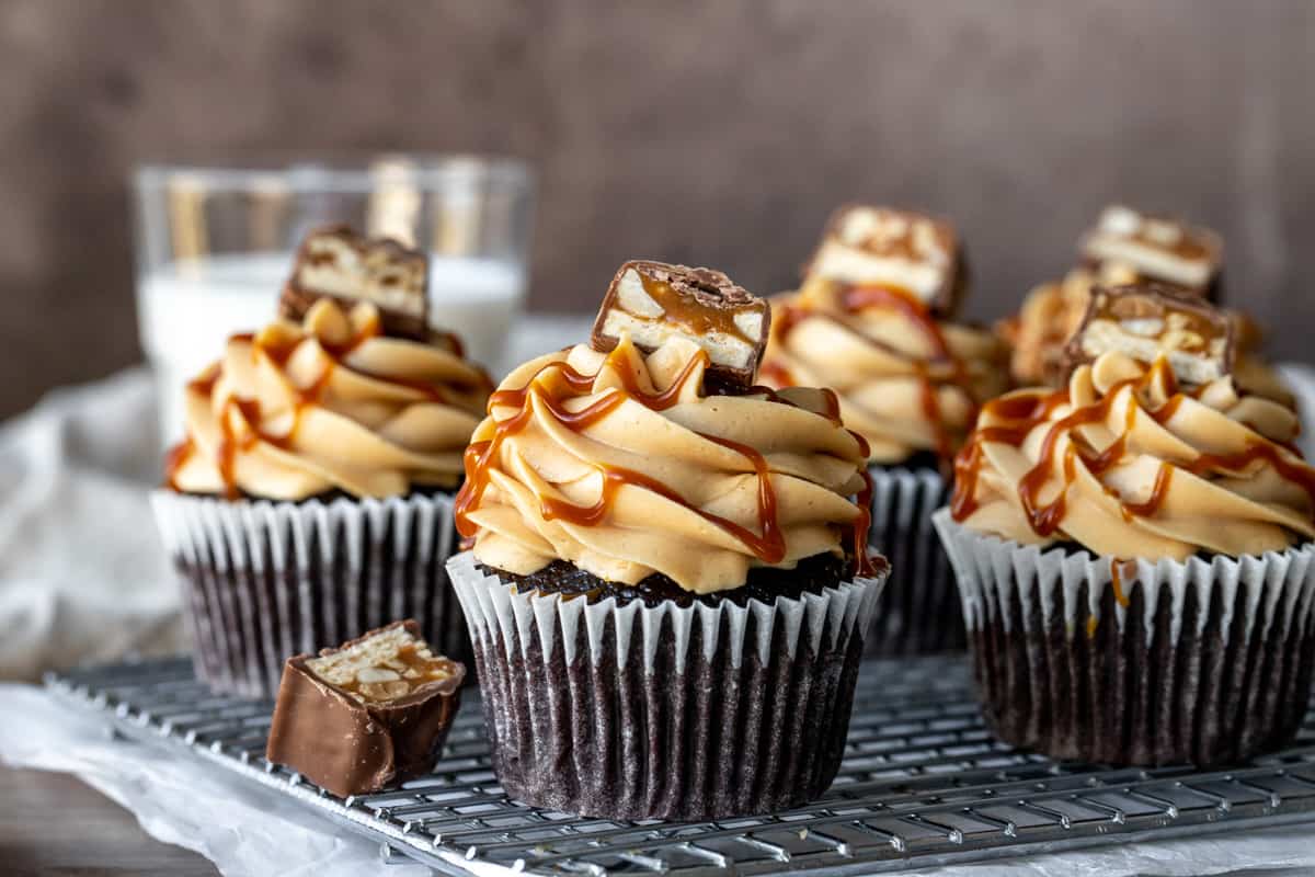 Cooling rack with chocolate cupcakes topped with peanut butter frosting and piece of snickers bar