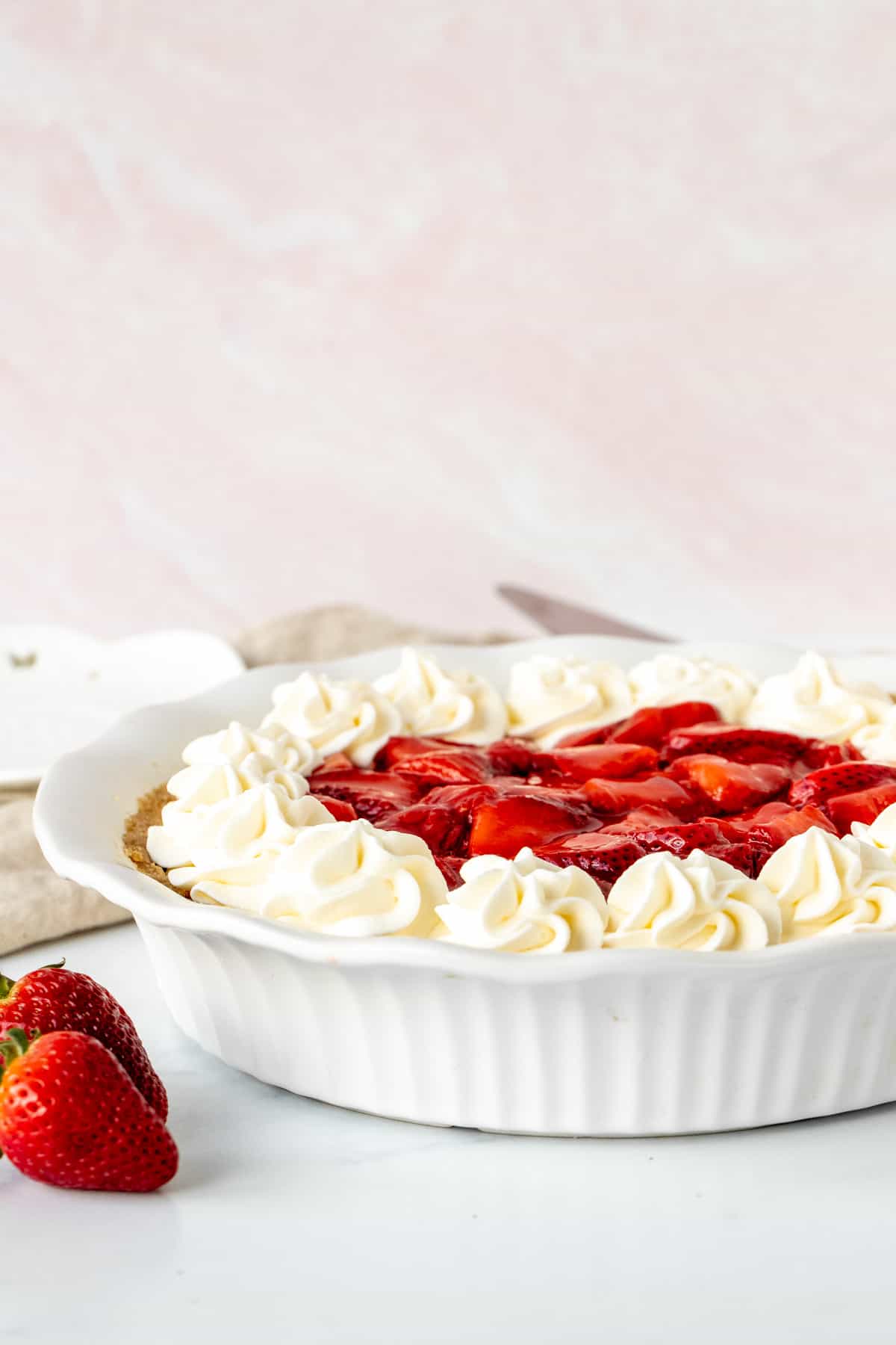 Strawberry cream cheese pie topped with whipped cream in a white pie plate
