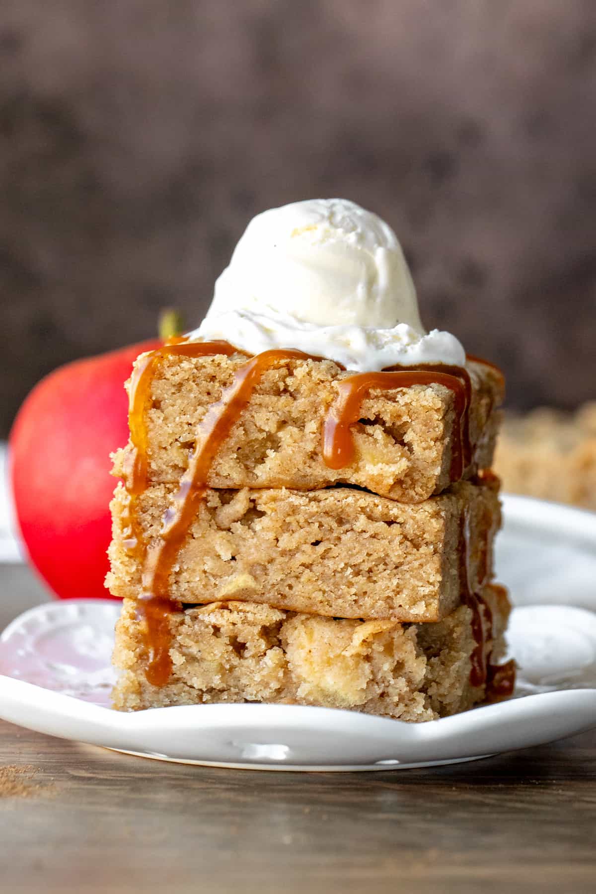 Stack of 3 caramel apple blondies on top of each other, topped with scoop of ice cream and drizzle of caramel