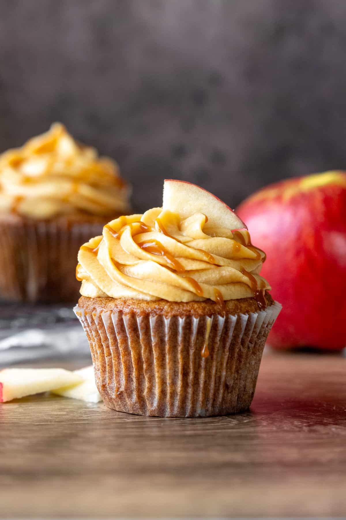 Caramel apple cupcake frosted with caramel frosting and topped with a drizzle of salted caramel and a slice of apple