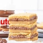Three Nutella stuffed blondies, one on top of each other with a jar of Nutella