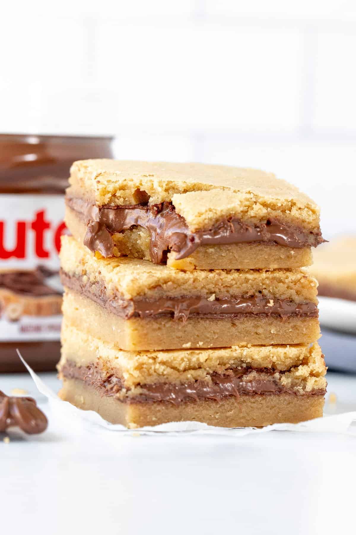 Stack of three Nutella blondies one on top of each other, with a bit taken out of the top blondie.