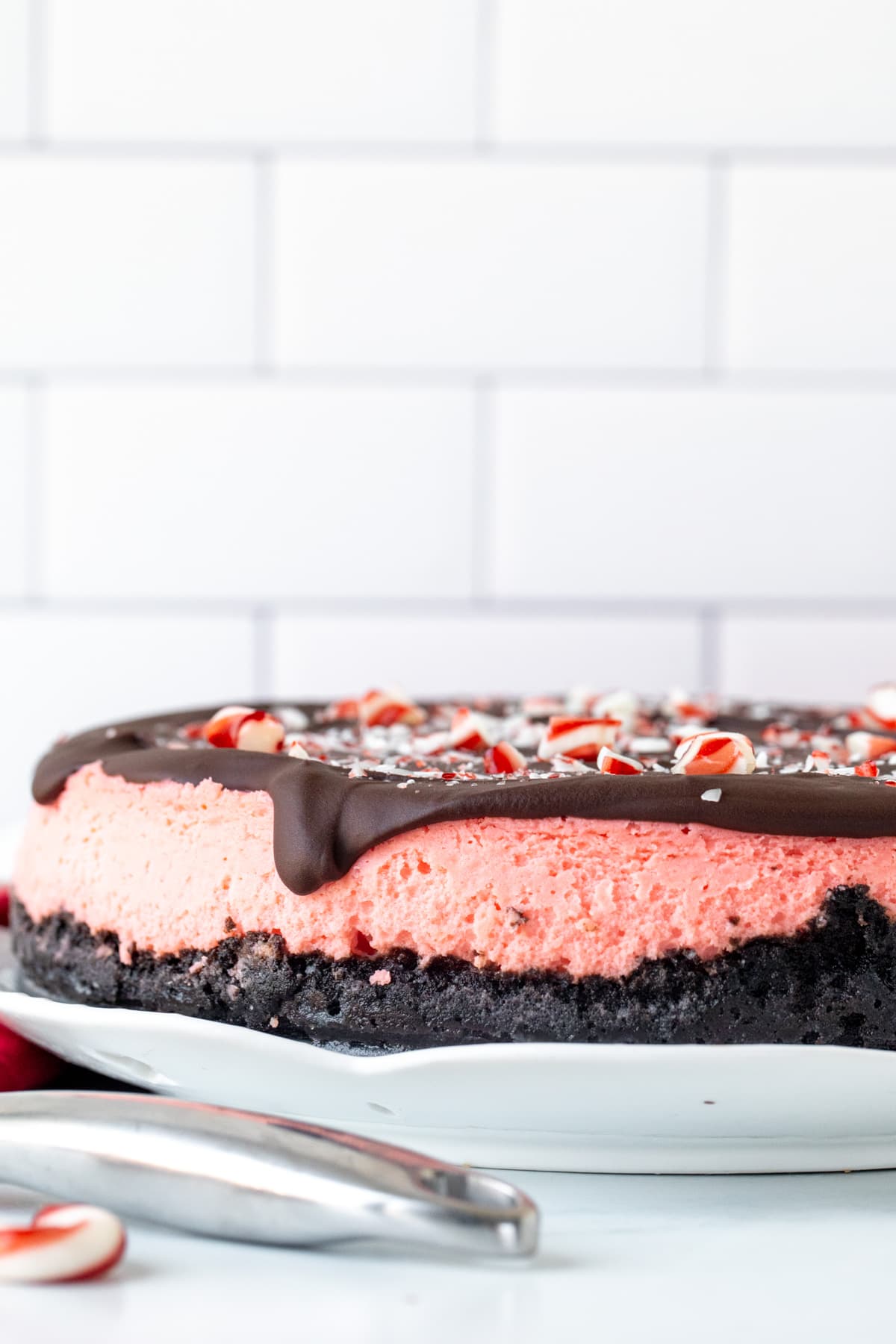 Round candy cane cheesecake with Oreo crust and chocolate topping on a white plate