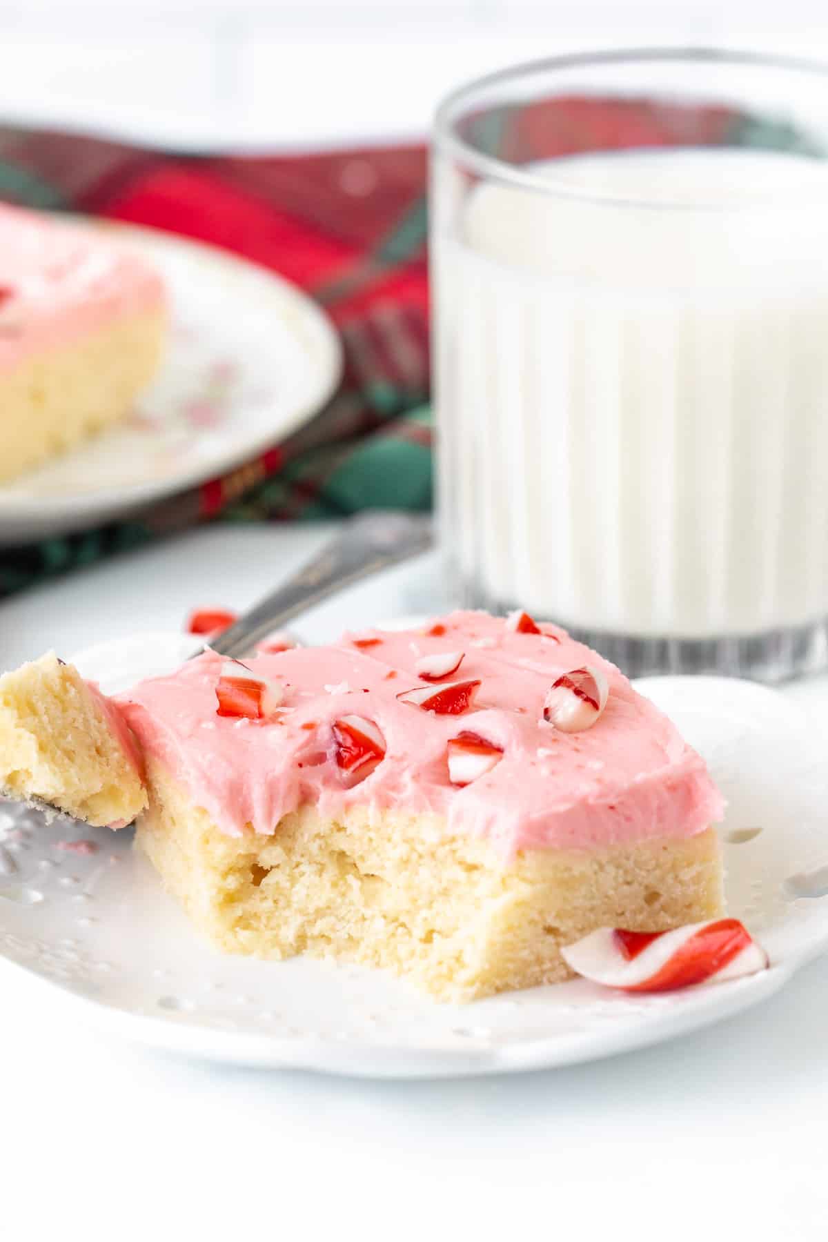 Candy cane sugar cookie bar with bite taken out, with glass of milk