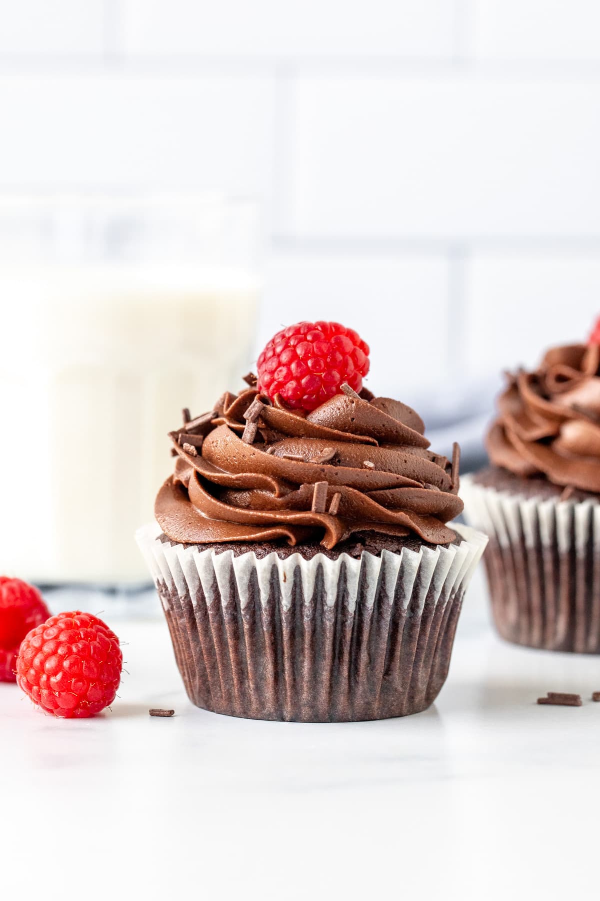 Chocolate cupcake with chocolate frosting and a raspberry on top with glass of milk