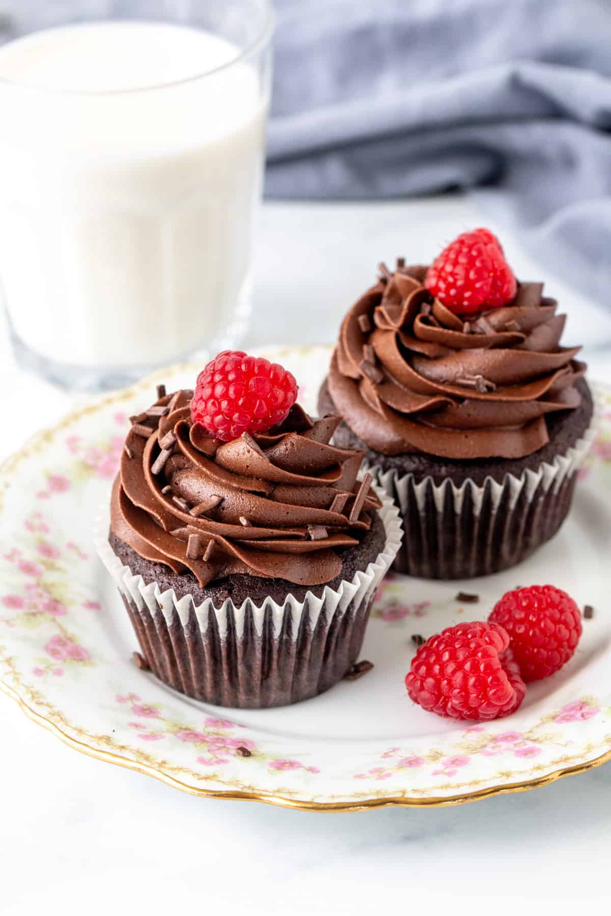Two chocolate cupcakes on a plate with glass of milk
