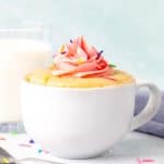 Vanilla mug cake decorated with pink frosting with a glass of milk