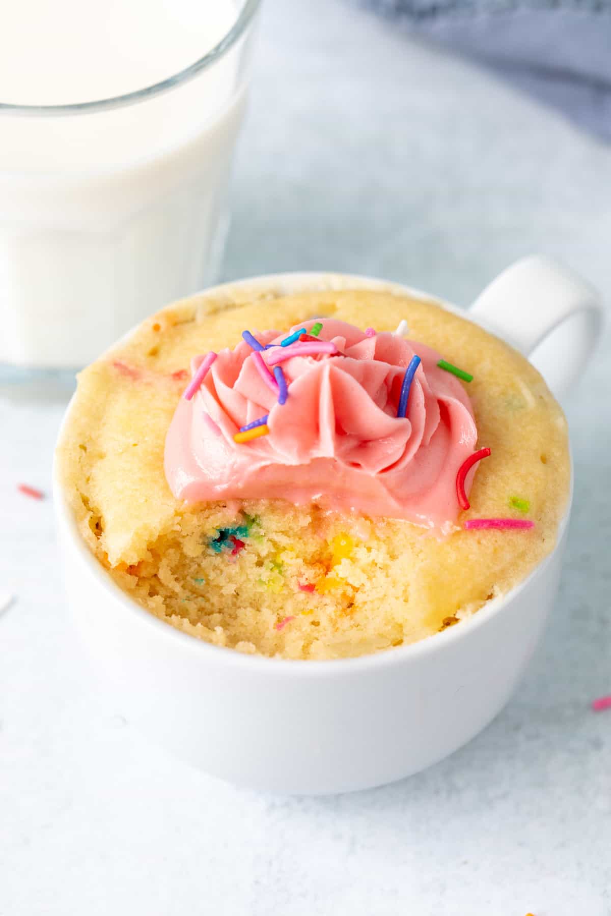 Sprinkle mug cake topped with vanilla frosting, with a spoonful taken out