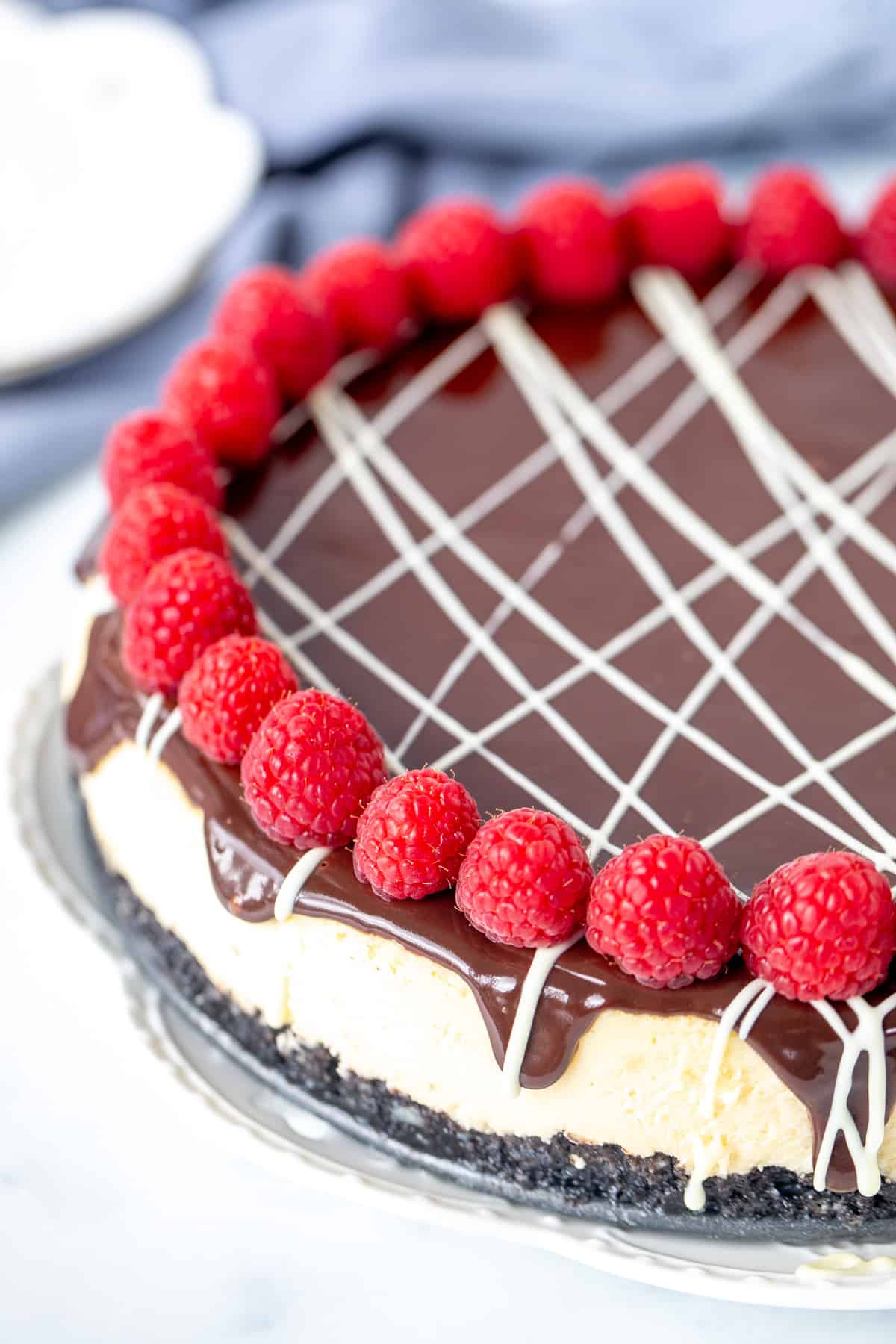 White chocolate cheesecake with chocolate topping, drizzle of white chocolate and reaspberries around the edges