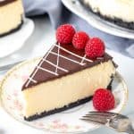 Piece of white chocolate cheesecake, topped with chocolate ganache & decorated with raspberries