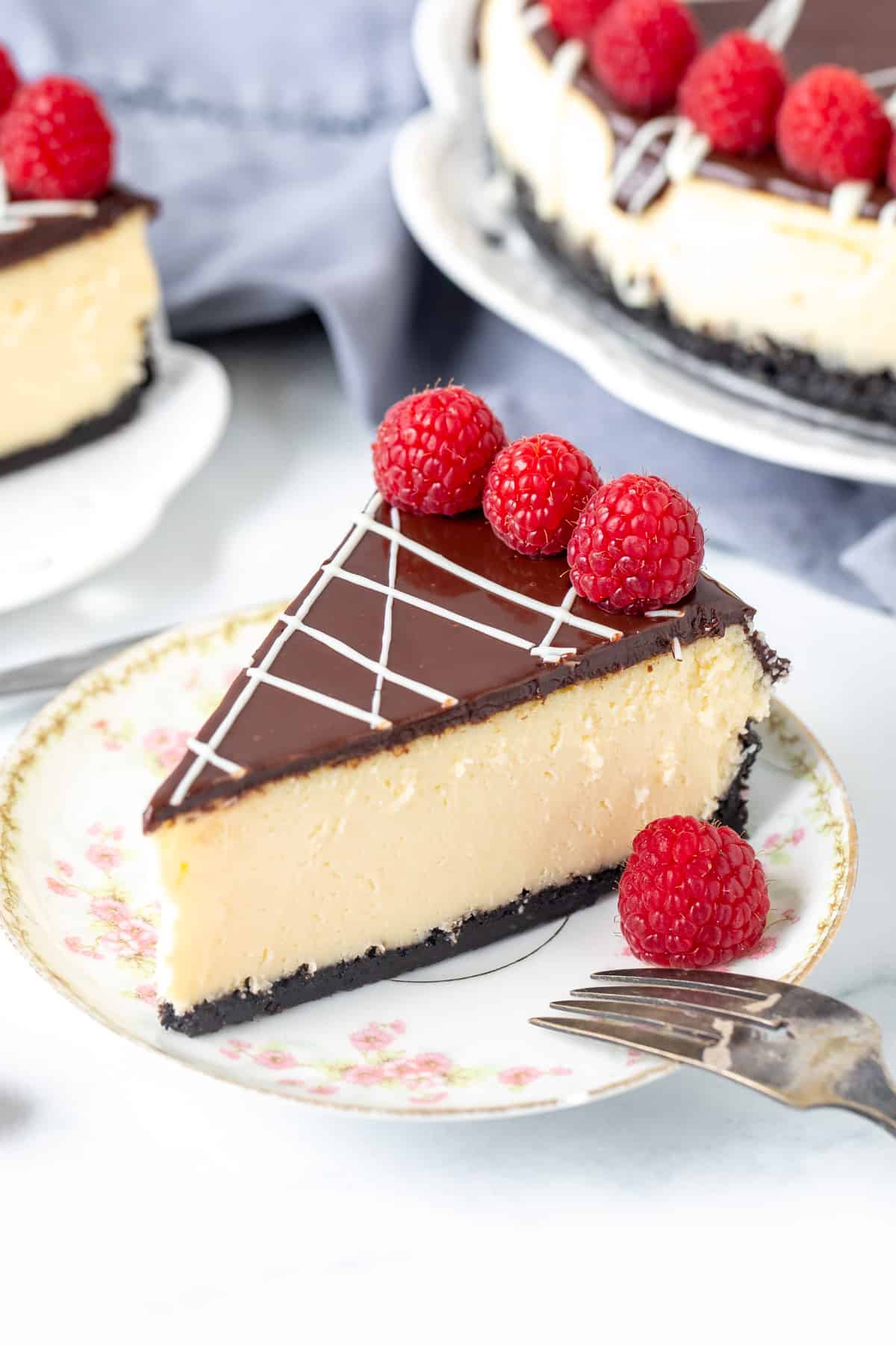 Piece of white chocolate cheesecake, topped with chocolate ganache & decorated with raspberries