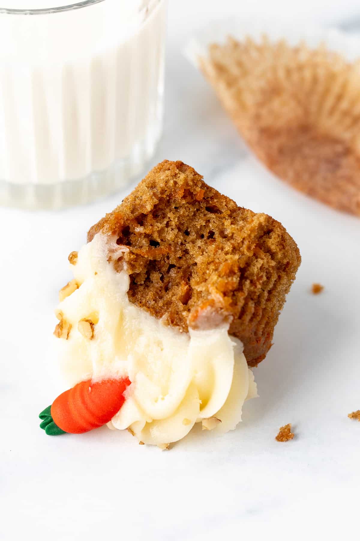 Carrot cake cupcake with a bite taken out, on its side with glass of milk