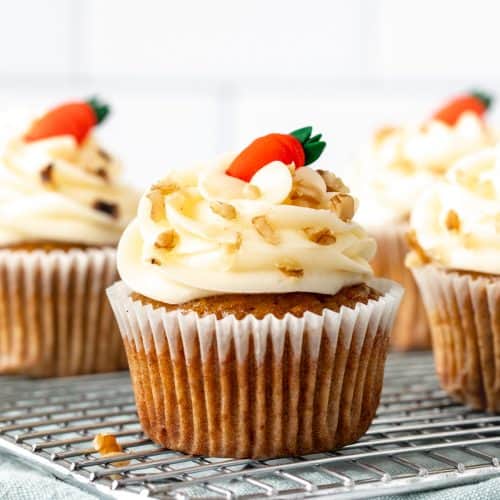 Carrot cake cupcakes topped with cream cheese frosting on a wire cooling rack