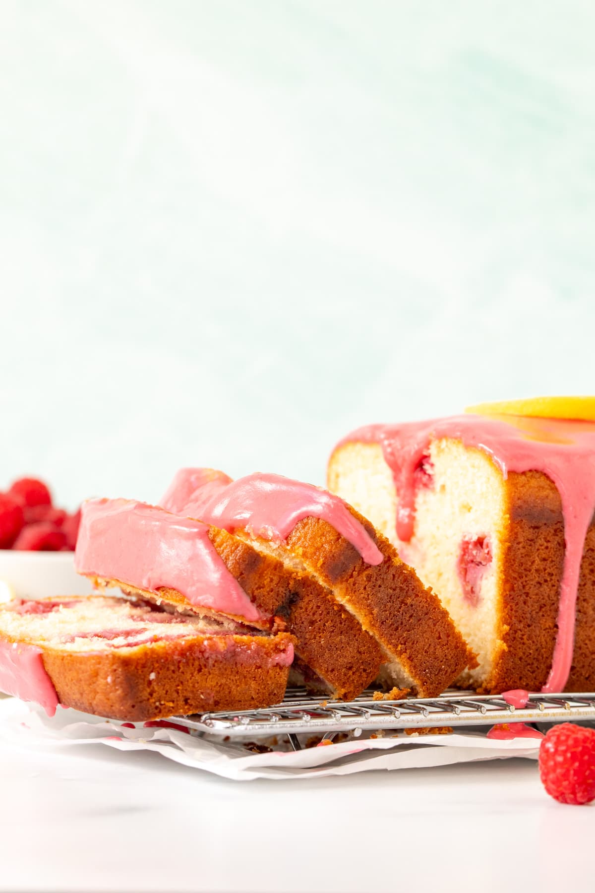 Lemon raspberry bread with pink raspberry glaze on a cooling rack with 3 slices cut.