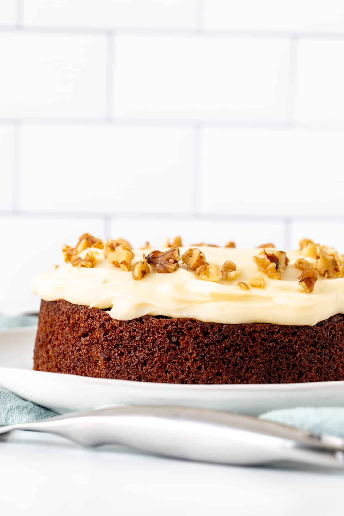 6-inch round carrot cake on a plate, topped with cream cheese frosting and walnuts