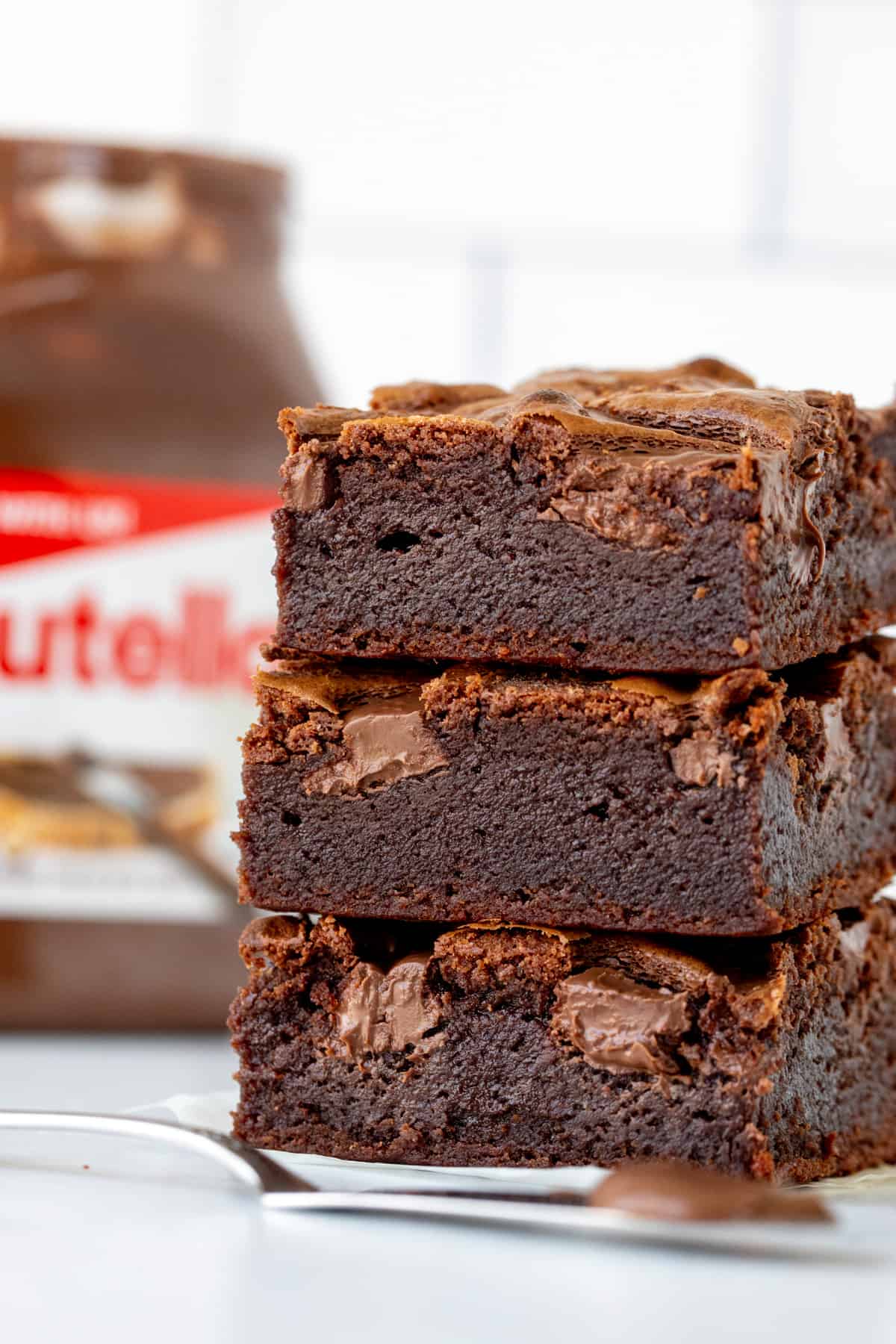 Stack of three Nutella brownies with jar of Nutella
