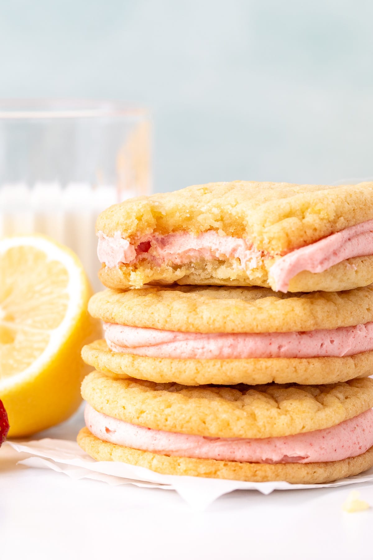 3 lemon sandwich cookies with strawberry frosting in the middle on top of each other, with a bite taken out of the cookie on top