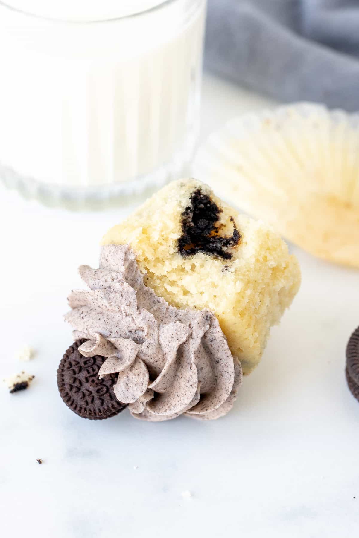 Oreo cupcake with a bite taken out, on its side with glass of milk